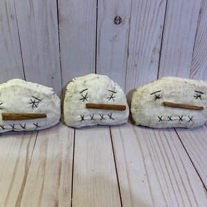 May include: Three handmade snowman ornaments. Each snowman is made of white fabric with black stitched eyes and mouth. A cinnamon stick serves as the nose. These rustic snowmen are perfect for winter or holiday decor.