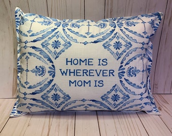 May include: Rectangular decorative pillow with a white background and a blue floral pattern. The pillow features the text "HOME IS WHEREVER MOM IS" in blue. The pillow has a soft, textured appearance.