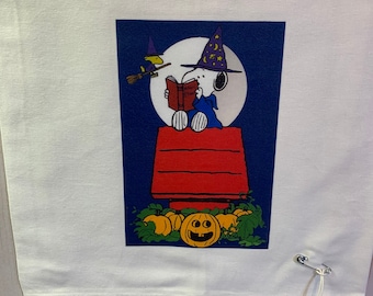 May include: White Halloween-themed fabric with a Snoopy graphic. Snoopy is dressed as a wizard, reading a book in front of a full moon. A witch on a broom flies above. Pumpkins and Snoopy's doghouse are also featured.
