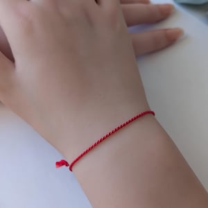 Peut inclure: Un bracelet en cordon rouge porté au poignet.