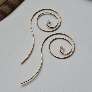 Könnte beinhalten: Ein Paar goldfarbene Drahtohhringe mit einem Spiraldesign. Die Ohrringe sind aus dünnem Draht gefertigt und haben einen zarten, minimalistischen Look.