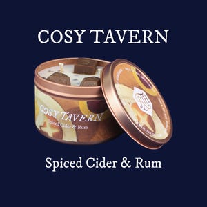 May include: A copper-colored candle tin with the text "COSY TAVERN" and "Spiced Cider & Rum". The lid is partially open, revealing the candle and several brown wax cubes. The background is a dark blue.