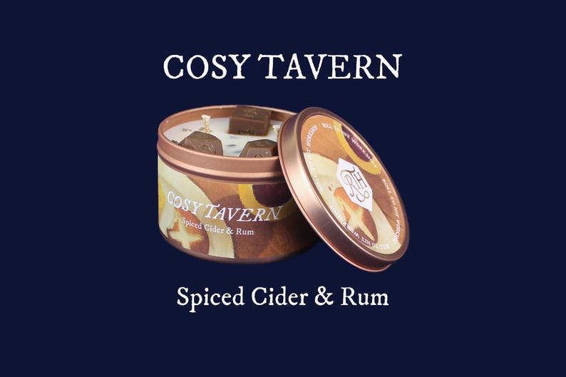 May include: A copper-colored candle tin with the text "COSY TAVERN" and "Spiced Cider & Rum". The lid is partially open, revealing the candle and several brown wax cubes. The background is a dark blue.