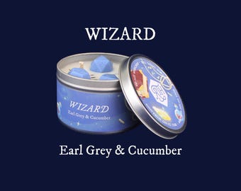 May include: A blue tin candle labeled "WIZARD Earl Grey & Cucumber" with a silver lid. The candle contains blue wax cubes. The lid is partially open, revealing a colorful design. The text "Earl Grey & Cucumber" is below the candle.