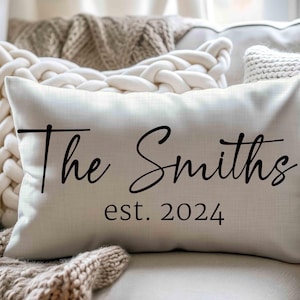May include: A rectangular off-white throw pillow featuring the black printed text The Smiths and est. 2024. The pillow has a smooth, woven fabric texture and is positioned horizontally, displaying a clear, centred personalised family name design.