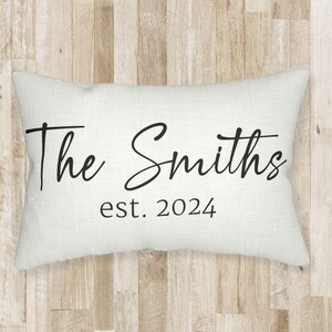 May include: A rectangular off-white throw pillow featuring black text printed on the front. The text reads The Smiths in a large cursive script font, with the smaller text est. 2024 printed directly underneath in a simple serif typeface.