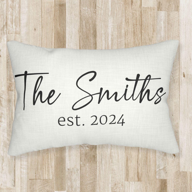 May include: A rectangular off-white throw pillow featuring black text printed on the front. The text reads The Smiths in a large cursive script font, with the smaller text est. 2024 printed directly underneath in a simple serif typeface.
