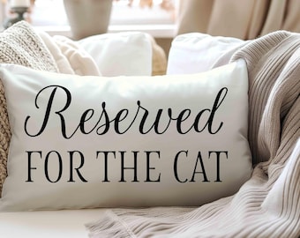 May include: A rectangular white throw pillow featuring the black printed text Reserved FOR THE CAT in a combination of elegant script and bold sans-serif lettering, centred on the front surface of the smooth fabric pillow cover.