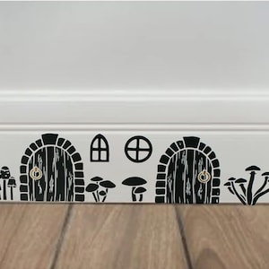 May include: Black and white wall decals featuring two small doors with round door knobs, a window, and a circle. The decals are arranged in a row along the baseboard of a white wall. There are also black and white mushroom decals on either side of the doors.