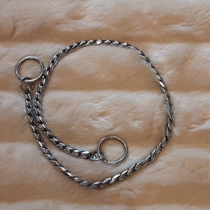 May include: A silver braided dog collar with two metal rings.