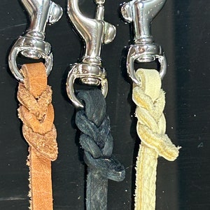 May include: Three leather dog leashes with silver swivel clips. The leashes are braided and come in brown, black, and cream.