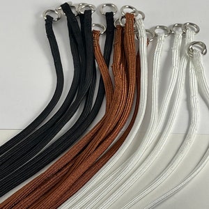 May include: A set of nine black, brown, and white cords with silver metal rings at the ends. The cords are arranged in a fan shape.