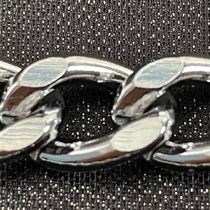 May include: Close-up of a silver chain link with a shiny, polished finish.