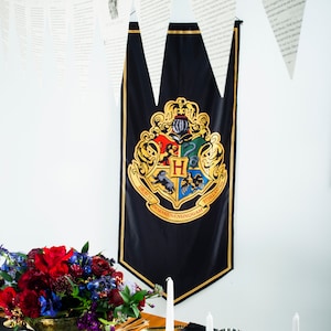 May include: Black banner with the Hogwarts crest, featuring a shield with four quadrants, each with a different animal and the letters "H", "DRACO", "DORMIENS", and "NUNQUIAM". The banner is hanging on a white wall.