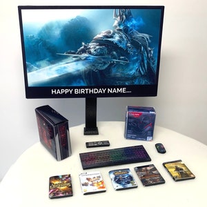 May include: A miniature gaming setup featuring a black computer monitor displaying a fantasy scene with the text "Happy Birthday Name..." A black computer tower, keyboard, and mouse are also included. Several video game cases are on a white surface.