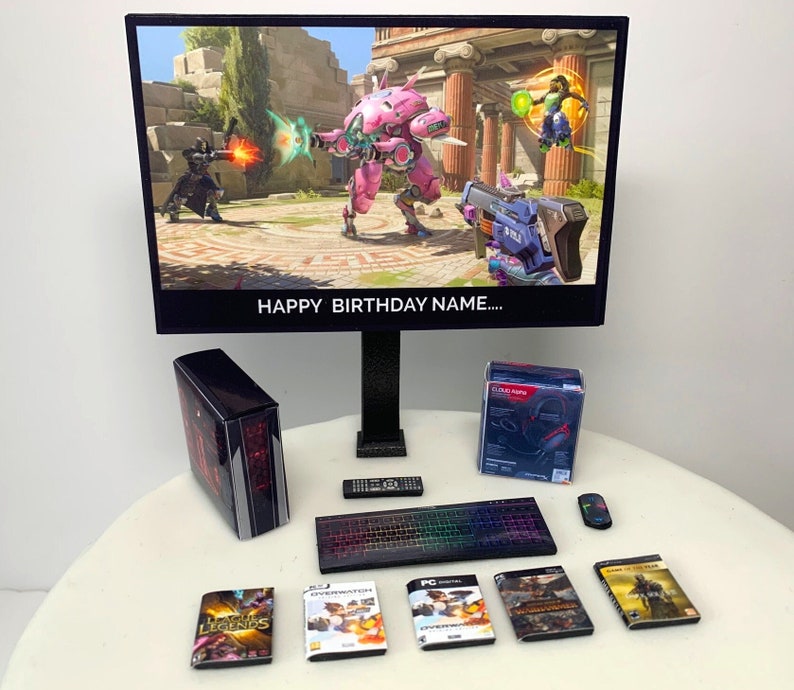 K&ouml;nnte beinhalten: Ein Computermonitor zeigt eine Videospielszene mit einem rosa Robotercharakter. Der Monitor steht auf einem St&auml;nder mit einem schwarzen Computergeh&auml;use, einer Tastatur, einer Fernbedienung und einem Headset. Der Text "Happy Birthday Name..." wird auf dem Monitor angezeigt.