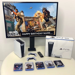 Peut inclure: Une console PlayStation 5 blanche et noire avec un disque de jeu, une manette et une télécommande. La console est sur une table blanche avec une manette de jeu blanche et noire et quatre étuis de jeux vidéo. L'arrière-plan est un mur blanc avec une image encadrée noire d'une scène de jeu vidéo. L'image porte le texte "Call of Duty Black Ops Cold War" et "Happy Birthday Name..."