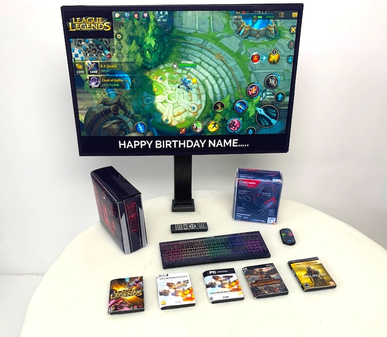 K&ouml;nnte beinhalten: Ein schwarzer Computermonitor mit einem League of Legends-Spiel auf dem Bildschirm. Der Bildschirm zeigt "Happy Birthday Name..." Ein schwarzer Computer-Tower, eine schwarze Tastatur, eine schwarze Fernbedienung, ein schwarzes Headset und mehrere Videospiel-H&uuml;llen befinden sich auf einer wei&szlig;en Oberfl&auml;che.
