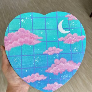 Könnte beinhalten: Ein herzförmiges Leinwandbild mit einem blauen und grünen Farbverlauf als Hintergrund. Der Hintergrund hat ein Gittermuster und ist mit rosa Wolken, weißen Sternen und einem weißen Halbmond verziert.