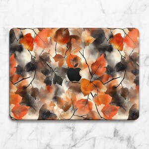 May include: Laptop skin featuring a watercolor design of autumn leaves in shades of orange, brown, and gray. The leaves are arranged with delicate black branches against a neutral background. The Apple logo is visible.