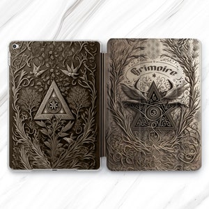 May include: A black and white iPad case featuring an intricate design of a triangle with a star inside, surrounded by vines and birds. The text "Grimoire" is written in a decorative font above the triangle.