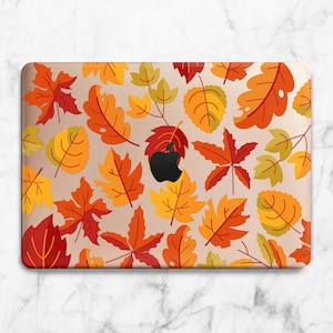 May include: A laptop case featuring a fall-themed design. The case is covered in various autumn leaves in shades of red, orange, and yellow. A black Apple logo is visible. The case is rectangular and fits a laptop.