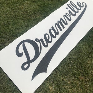 May include: White yoga mat with black text that reads "Dreamville" in a stylized baseball font.