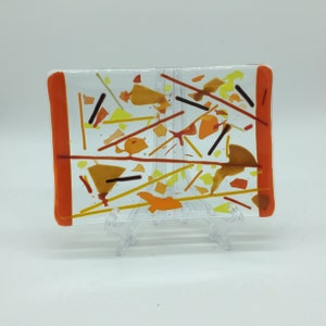 May include: A rectangular glass dish with an orange border and a colorful abstract design featuring yellow, orange, and brown glass pieces.