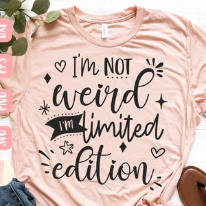 Peut inclure: Un t-shirt rose avec le texte "I'm not weird I'm limited edition" en lettres noires. Le texte est entouré de petits cœurs, étoiles et diamants.