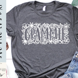 May include: A dark grey t-shirt with a white floral design and the word "Grammy" in the centre.