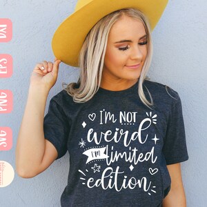 May include: A woman wearing a dark gray t-shirt with the text "I'm not weird I'm limited edition" in white. The shirt has a white heart, star, and diamond design.