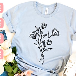 May include: A light blue t-shirt featuring a black line drawing of a bunch of flowers. The flowers have five petals each and are arranged in a cluster.