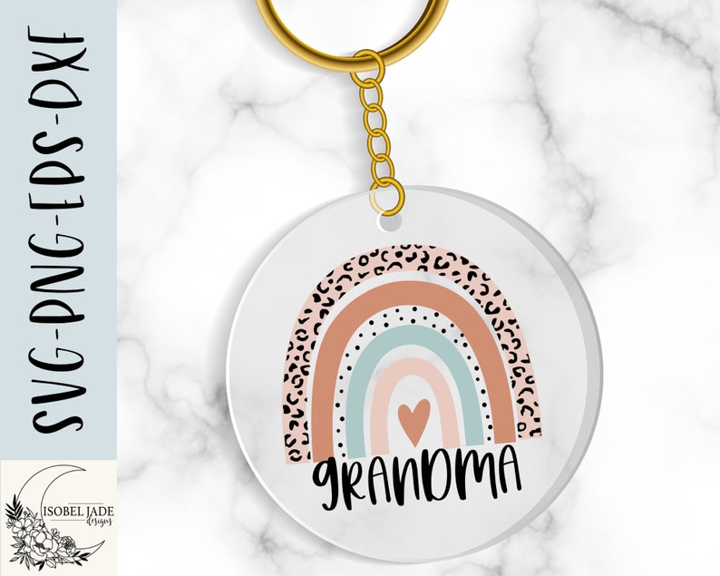 May include: A white circle keychain with a rainbow design and the word "Grandma" in black text. The rainbow has a pink, blue, and white color scheme with a black and white leopard print pattern.