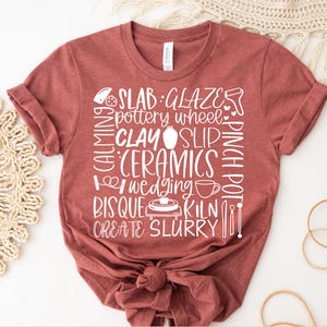 Op de afbeelding: Een terracotta-kleurig t-shirt met witte tekst en illustraties gerelateerd aan pottenbakken. De tekst bevat woorden als "SLAB", "GLAZE", "CLAY" en "CERAMICS". Het shirt is aan de onderkant geknoopt. De woorden "INSTANT ACCESS" en "DIGITAL DOWNLOAD" staan bovenaan en onderaan.