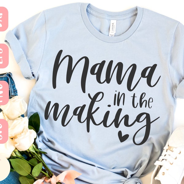 Könnte beinhalten: Ein hellblaues T-Shirt mit dem Text "Mama in the making" in schwarzer Kursivschrift mit einem kleinen Herz unter dem Text.