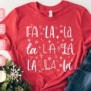 以下が含まれることがあります： 白い文字で「FA LA La la LA LA LA LA La」と書かれた赤いTシャツ。文字の周りは小さな星と雪の結晶で囲まれています。