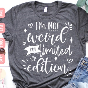 May include: A gray t-shirt with the text "I'm not weird I'm limited edition" in white. The text is surrounded by small hearts, stars, and diamonds.