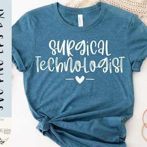May include: A teal blue t-shirt with the text "Surgical Technologist" in white script font. A small white heart is centred below the text.