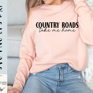May include: A pink sweatshirt with the text "COUNTRY ROADS take me home" in black lettering.