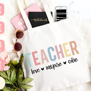 Może przedstawiać: Biała torba z napisem "TEACHER" w kolorowych literach. Poniżej słowa "love inspire care" ze znakami serca. Torba zawiera r&oacute;żowy notatnik, czarny notatnik, okulary przeciwsłoneczne i smartfon.