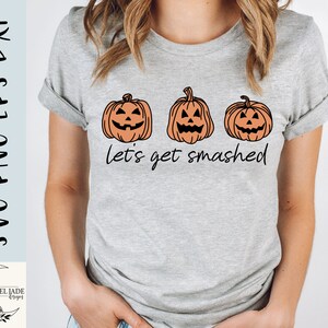 Puede incluir: Una camiseta gris con tres caras de calabaza naranja y el texto "Let's get smashed".
