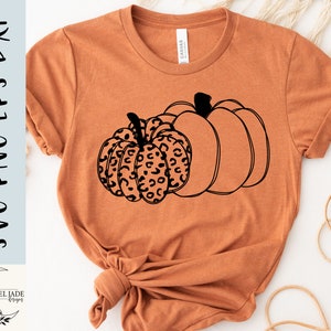 May include: A brown t-shirt with a black outline of two pumpkins. One pumpkin has a leopard print pattern.