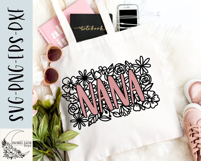 May include: A white tote bag with a black floral design and the word "NANA" in pink lettering. The bag is lying on a white surface with other items, including a notebook and a phone.