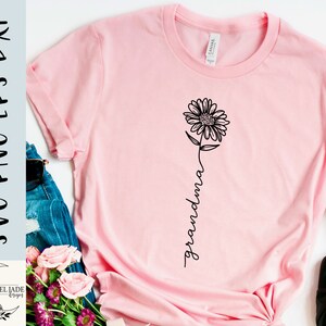 May include: Pink t-shirt with a black outline of a sunflower and the word "grandma" written vertically.