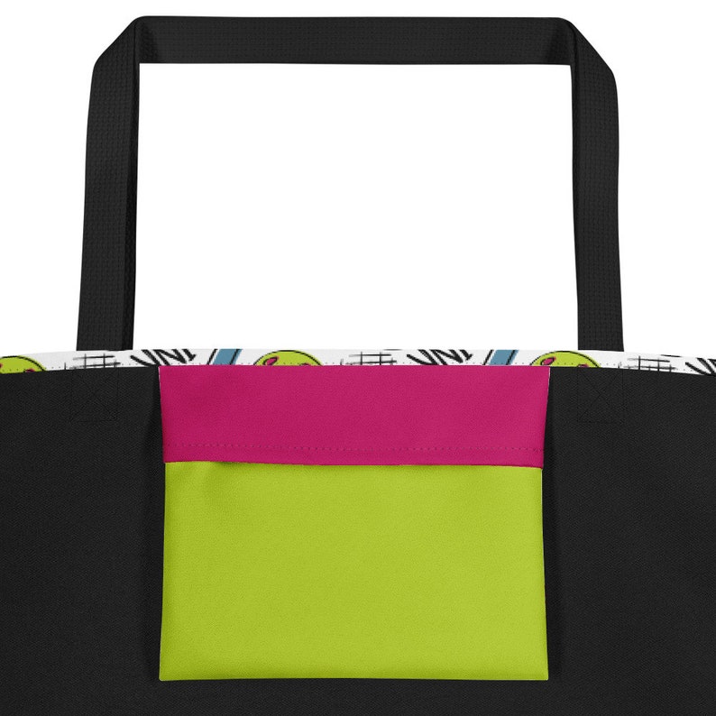 Op de afbeelding: Zwarte tote bag met een roze en groene zak. De tas heeft een witte voering met een kleurrijk patroon.