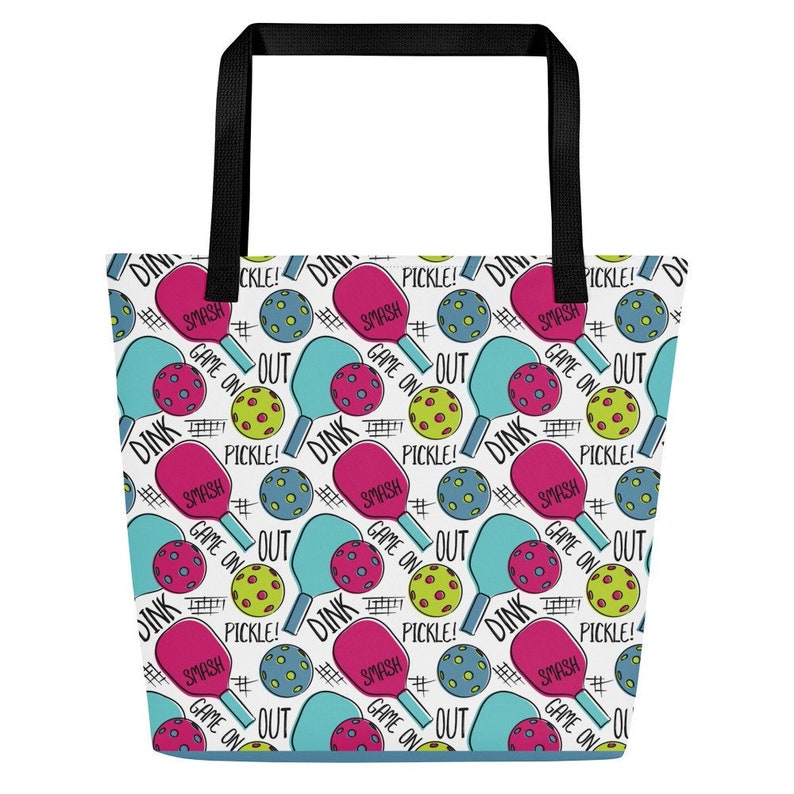 Op de afbeelding: Een witte tote bag met een kleurrijk patroon van pickleball-rackets, ballen en de woorden "Dink", "Smash", "Game On", "Pickle!" en "Out".