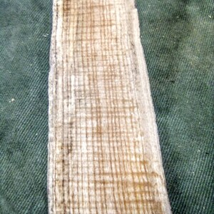 May include: A close-up of a piece of wood with a light brown color and a grain pattern. The wood has a rough texture and appears to be weathered.