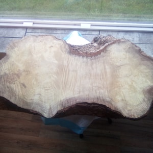 May include: A large, natural wood slice with a light brown color and a unique, irregular shape. The wood has a beautiful grain pattern and a rough, textured surface.