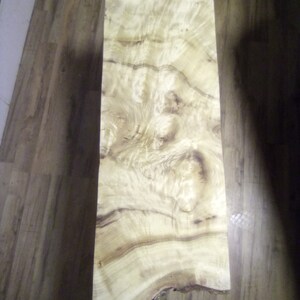 May include: A large piece of wood with a natural, light brown color and a unique, swirling grain pattern. The wood has a live edge and is suitable for crafting furniture or other woodworking projects.