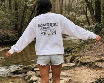 Mockup de moletom branco Gildan 18000 com gola redonda, vista traseira, estilo de vida na natureza, floresta, córrego rural, estética de vestuário para atividades ao ar livre.